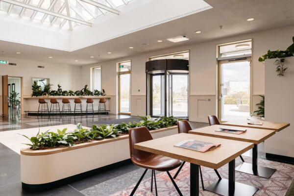 Moderne en lichte ontvangsthal aan de Fascinatio Boulevard met plantenbakken, zithoeken en een draaideur.